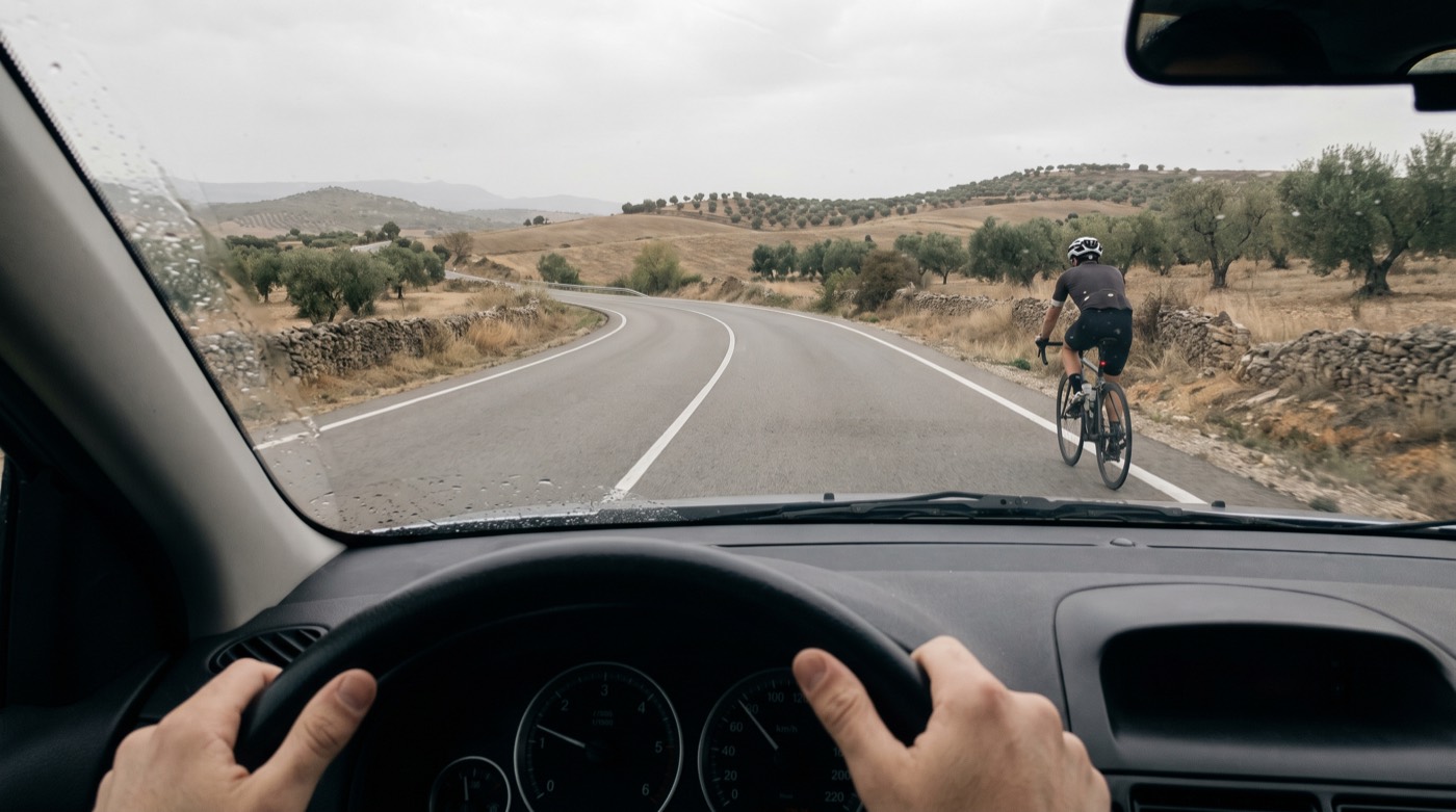 Vista desde el interior de un coche que se acerca a un ciclista en una carretera convencional